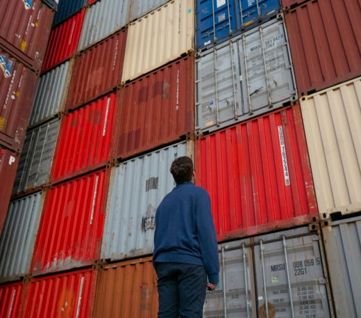 man in blue long sleeve shirt standing in front of red and blue intermodal containers